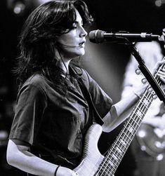 a woman holding a guitar while standing in front of a microphone