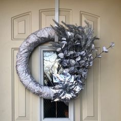 a wreath is hanging on the front door of a house with flowers and leaves wrapped around it