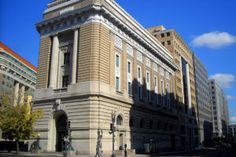 an old building in the middle of a city with tall buildings on both sides and blue skies above