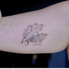 a woman's arm with an inked oak leaf and acorn tattoo on it