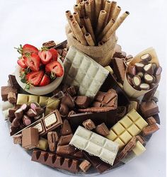 a platter filled with assorted chocolates, strawberries and other treats on top of a white table