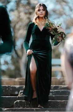 a woman in a green dress is walking down some steps with her leg up and holding flowers