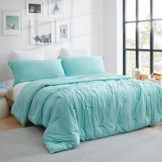 a bed with blue comforters and pillows in a room next to a large window