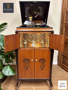 an old fashioned record player is sitting on top of a wooden cabinet in front of a potted plant