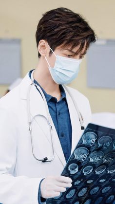 a male doctor in a white coat and mask is looking at an x - ray