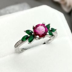 This beautiful ring is made from genuine 925 sterling silver with rhodium plating. Ring details- -The Main stone is a round cut 6mm Lab Created Ruby Stone -Side stones are 4mm by 2mm Lab Emerald Marquise and 1mm Round simulated diamonds -Ring is casted in solid 925 sterling silver with rhodium plating (yellow gold and rose gold plated also available, please check the drop down menu for more options) -The Total face height of the ring measures 7mms and the band width measures 1.5mms -Each ring is Silver Round Emerald Promise Ring, Emerald Ring With Cubic Zirconia And Accent Stones, Silver Emerald Ring With Center Stone, Round Emerald Ring With Cubic Zirconia Accent Stones, Cubic Zirconia Emerald Ring With Birthstone, Cubic Zirconia Emerald Ring With Accent Stones, Sterling Silver Flower Ring With Round Cut, May Birthstone Crystal Ring With Accent Stones, Fine Jewelry Round Flower Ring With May Birthstone