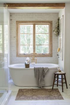 a white bath tub sitting under a window next to a wooden stool in a bathroom