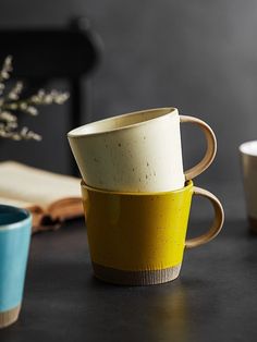 three coffee cups sitting on top of a table next to an open book and vase