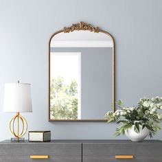 a vase with flowers on top of a dresser next to a large mirror and lamp