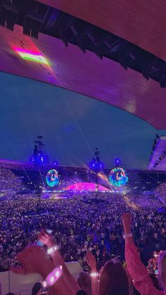 a large crowd at a concert with their hands up in the air and lights on