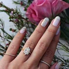 a woman's hand with two different rings on it and flowers in the background