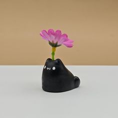 a small black cat with a pink flower in it's mouth