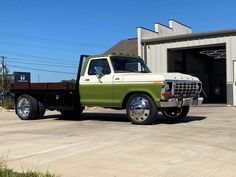 a green and white truck parked in front of a building with an open garage door