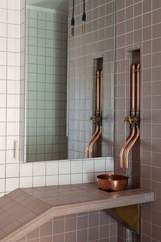 a bathroom with pink tiles and copper fixtures on the wall, along with a mirror