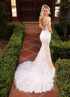 a woman in a white wedding dress standing on a brick walkway with hedges and bushes