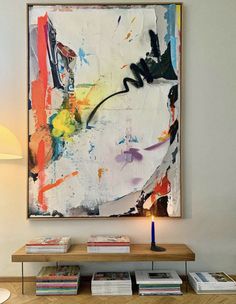 an abstract painting hangs on the wall above a coffee table with books and a lamp