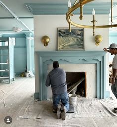 two men are working on a fireplace in a room with blue walls and white paint