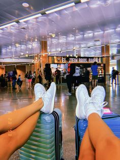 two people sitting on suitcases in an airport terminal with their feet propped up against each other