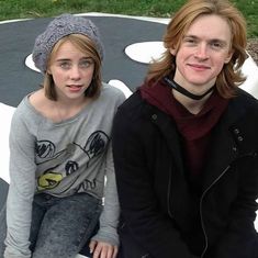 two young people sitting on top of a black and white bench in front of a playground