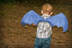 a little boy holding a blue bat in his hands and looking at the ground with it's wings spread