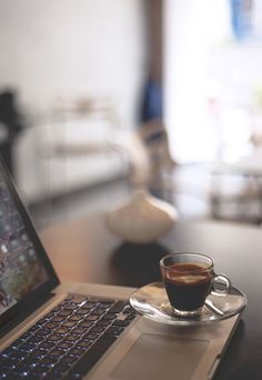 a laptop computer sitting on top of a wooden table next to a cup of coffee