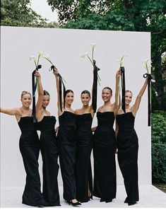 four women in black dresses are holding flowers and posing for the camera with their arms up