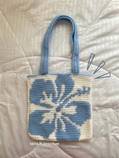 a crocheted blue and white bag sitting on top of a bed next to four knitting needles