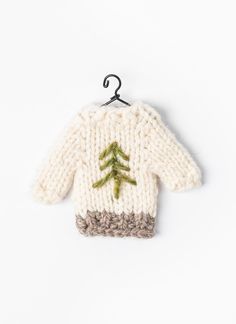 a knitted sweater hanging from a hook on a white wall with a green tree embroidered on it