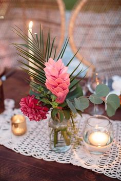 a table topped with a vase filled with flowers next to candles and greenery on top of a white doily