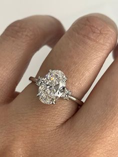 a woman's hand with an oval diamond ring on it, and the center stone is