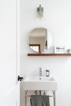 a white sink sitting under a bathroom mirror next to a wooden shelf with towels on it