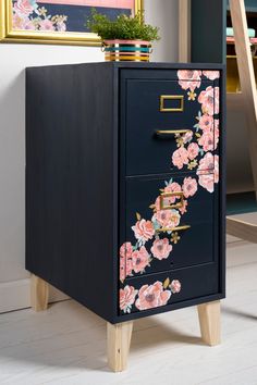 a black cabinet with pink flowers painted on the front and bottom drawers, next to a ladder