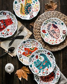 four plates with designs on them sitting on a table next to some knitting needles and yarn