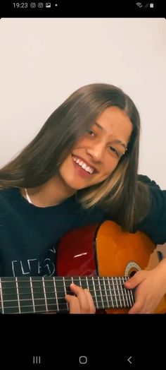 a woman with long hair is playing an acoustic guitar and smiling at the camera,