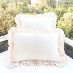 two white pillows sitting on top of a bed next to each other near some trees