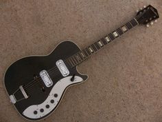 a black and white guitar laying on top of a carpeted floor next to a wall