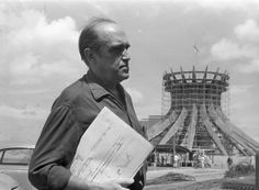 an older man holding papers in front of a roller coaster