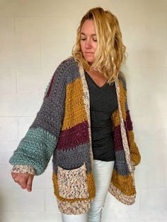 a woman standing in front of a white wall wearing a multicolored cardigan