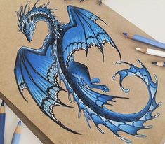 a drawing of a blue dragon sitting on top of a piece of paper next to colored pencils