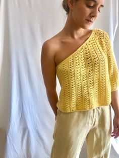 a woman standing in front of a white backdrop wearing a yellow knitted top with one shoulder