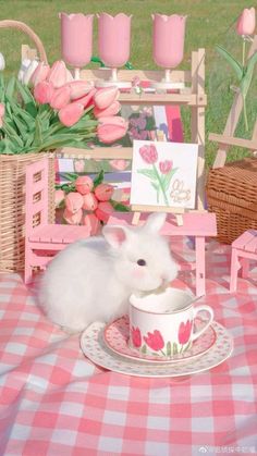 a small white hamster sitting in a teacup on a table with pink flowers