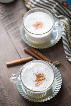 two mugs filled with hot chocolate sitting on top of a wooden table next to cinnamon sticks