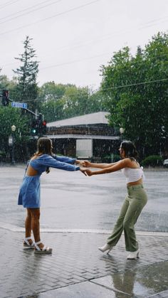 two young women playing in the rain with an umbrella over their heads and one holding out her hand