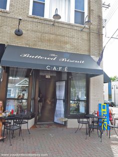 the outside of a restaurant with tables and chairs on brick sidewalk next to tall building