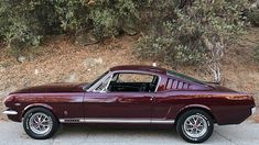 a maroon car parked on the side of a road next to some bushes and trees