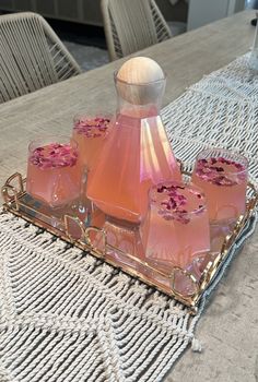 four glasses on a tray with pink liquid in them sitting on a dining room table