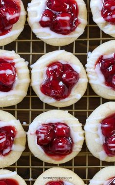 several cookies with white frosting and cherry toppings on a cooling rack, ready to be eaten