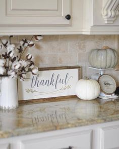 a kitchen counter topped with lots of white pumpkins and cotton flowers next to a sign that says, thank