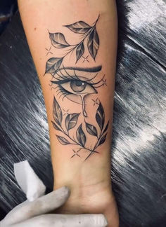 a woman's arm with an eye and leaves tattoo on it