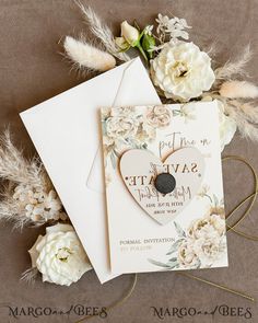 wedding save the date cards with flowers and feathers on them next to some white carnations